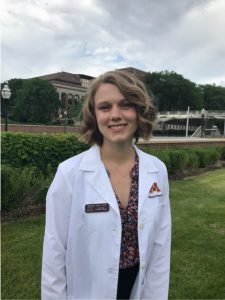 Meghan Soler stands on the University of Minnesota's campus wearing a white lab coat.